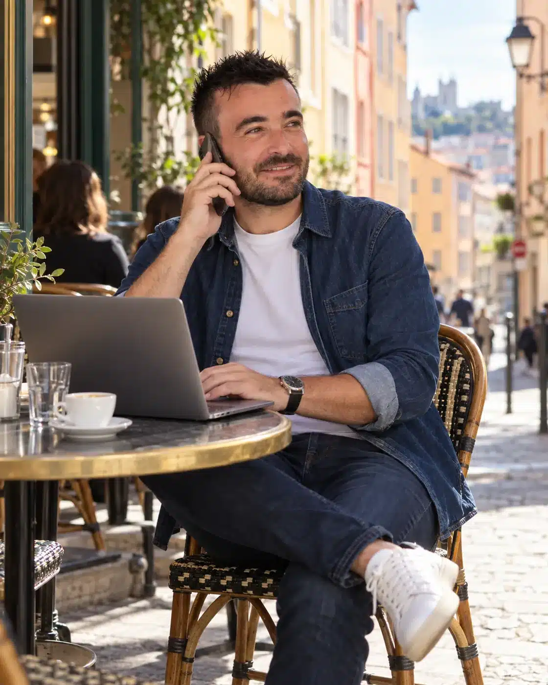 Florian Caux, consultant SEO à Lyon, au téléphone avec un client à la terrasse d'un café des pentes de la Croix-Rousse, ordinateur portable ouvert